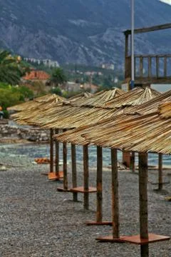 Row of the straw sun umbrellas on empty beach in Montenegro Stock Photos