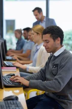 Row of students using computers teacher watching over them Stock Photos