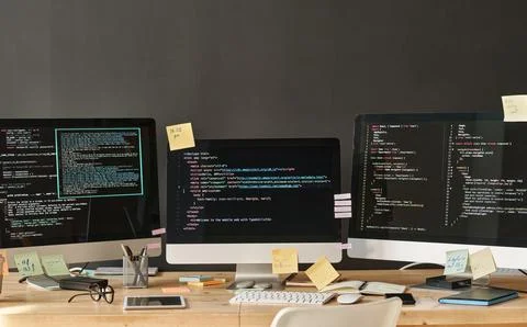 Row of three computer monitors with coded data on screens standing on table Foto stock