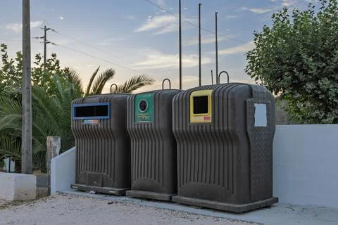 A row of three large, plastic recycling bins in blue, green, and yellow stand Foto stock