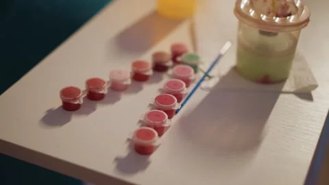 Row Of Tiny Paint Pots On Canvas Beside Blue Brush And Mixing Cup, Neat Lineup Stock Footage 323922353