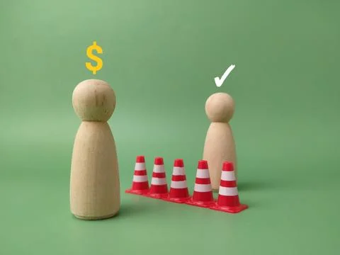 A row of traffic cones separates two wooden figures, one with a dollar sign.. 库存照片
