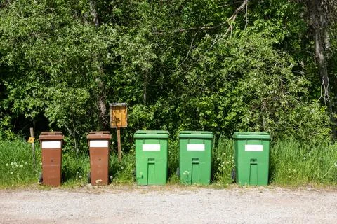 Row of trash bins aligned along a path near woods in the countryside Stock Photos
