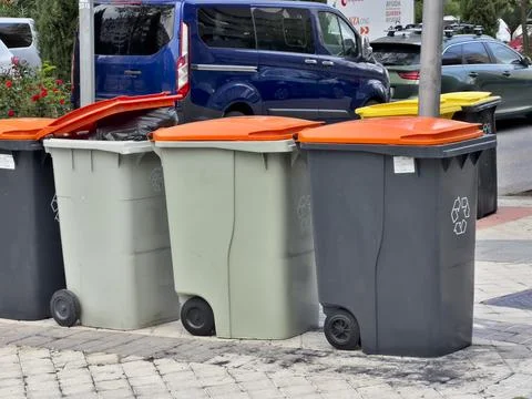A row of trash cans are lined up on the sidewalk Stock Photos