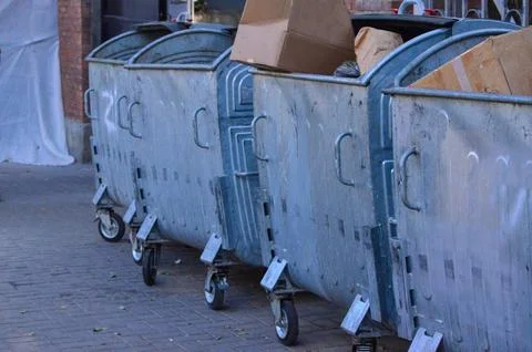 A row of trash cans are lined up on the sidewalk. Stock Photos