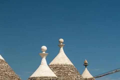 Row of trullo conical rooftops with white spherical pinnacles against clear blue Stock Photos