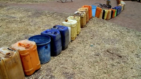A row of various colorful plastic jerrycans and buckets lined up on dry Stock Footage 345835183