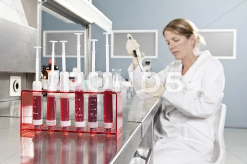 A row of vials holding blood and a lab technician working in background, focus Stock Photos