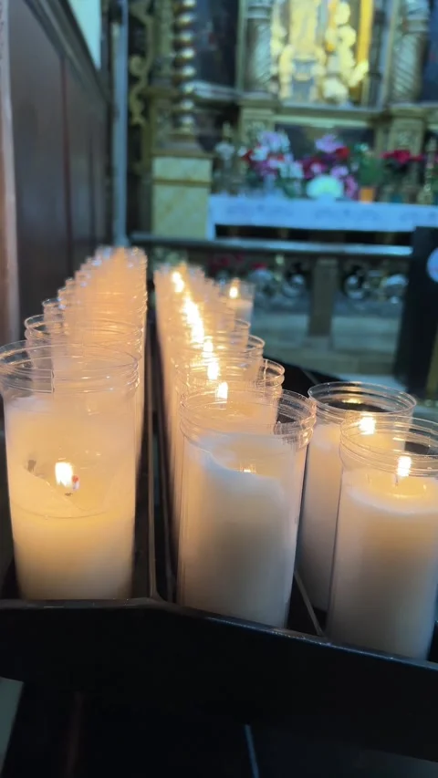 Row of white devotional candles burning in glass holders inside historic church Vidéo 326465581