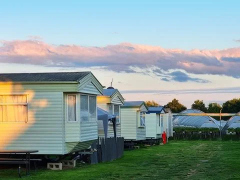 A row of white mobile homes sit in a grassy field Stock Photos