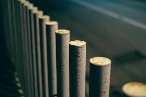 Row of white piles that divide the sidewalk from the road where cars pass Stock Photos