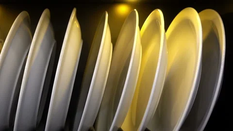 Row of white plates on a stand in a light bulb on black Stock Footage 87195901
