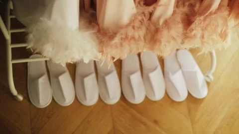 Row of white spa slippers under pastel feather bridal robes, wedding morning Stock Footage 328770467