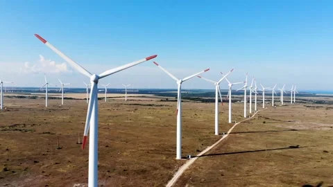 Row of white wind turbines spinning synchronously in a field on blue sky backgro Stock Footage 220081689