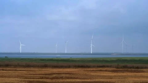 Row of wind turbines generating clean green energy near coast behind agricu.. Vídeo Stock 338198019
