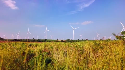 Row of wind turbines rising over a rural field beneath a clear blue sky Stock Footage 330159452