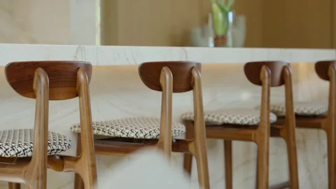 Row of wooden bar stools with patterned cushions placed along marble countertop Stock Footage 297751637