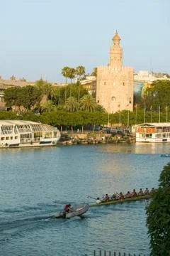Rowers row by octagonal tower of Torre del Oro makes golden reflection on Canal Stock Photos