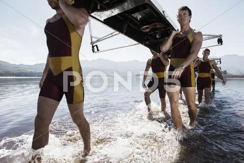 Rowing team carrying scull out of lake Stock Photos