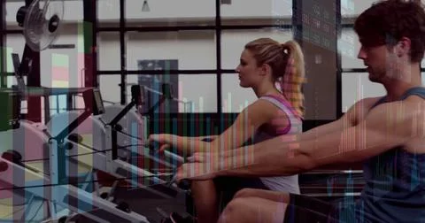 Rowing workout partners using rowing machines at modern gym, with wall fan and Stock Photos