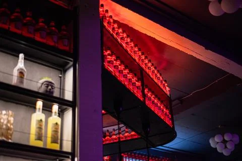 Rows of Aperol bottles on a curved shelf illuminated by red neon light in a bar Stock Photos