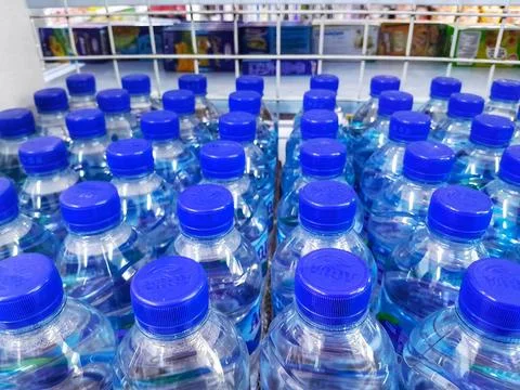 Rows of blue cap plastic bottles with drinking water in the minimart. Stock Photos