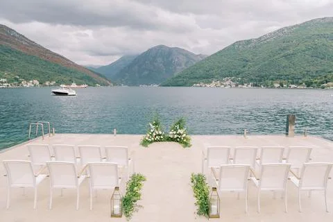 Rows of chairs stand on the pier in front of a floor wedding arch Stock Photos