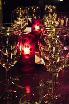 Rows of clean, empty wine glasses on a table, candle lights between Stock Photos