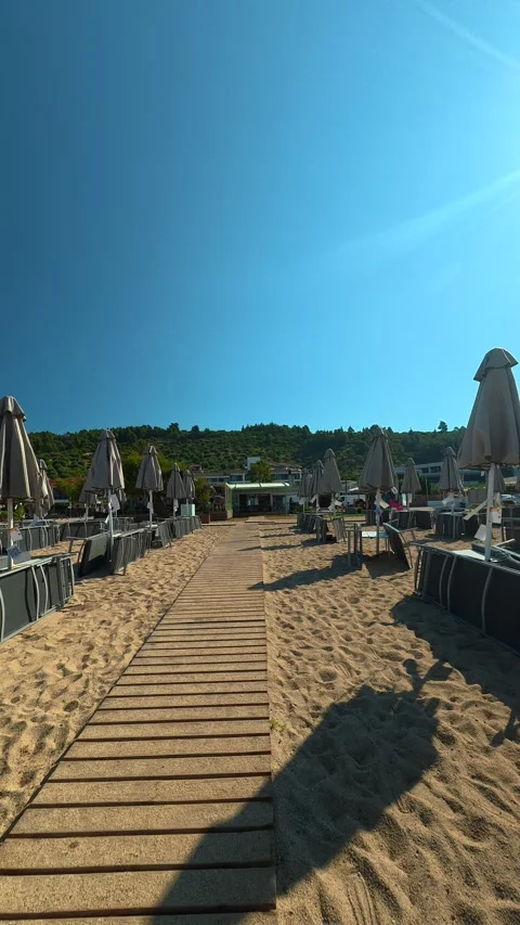 Rows of closed umbrellas line the quiet beach. Lagomandra, Greece. Vertical Stock Footage 339630450