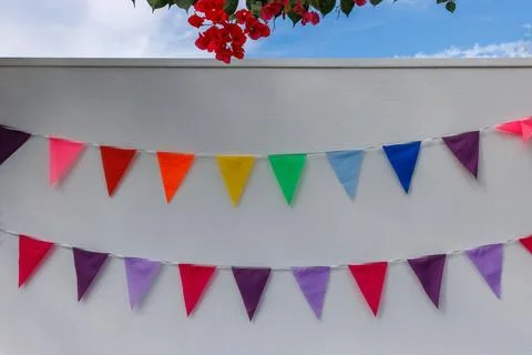 Rows of colorful triangular bunting flags hanging on a textured white wall,.. Stock Photos