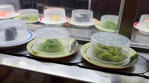 Rows of covered sushi plates move along a conveyor belt in a Japanese resta.. Stock Footage 338133142