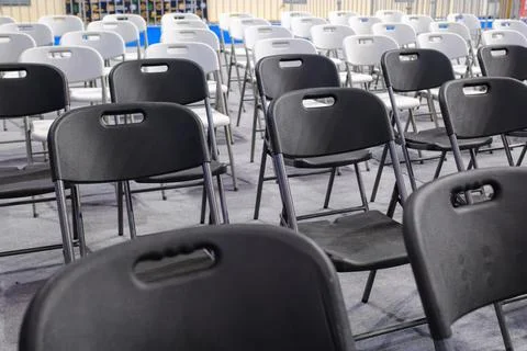 Rows of empty black and white plastic folding chairs in an event hall Stock Photos