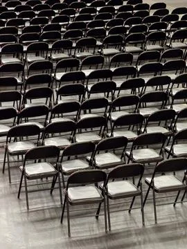 Rows of empty black folding chairs on a grey floor for an event or conference Stock Photos