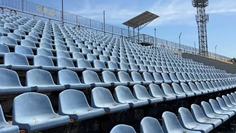 Rows of empty blue plastic stadium seats sit under a bright sky Stock Footage 312400678