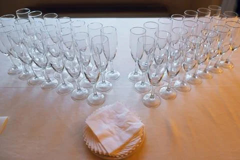 Rows of empty champagne flutes arranged on a table with a stack of napkins Stock Photos