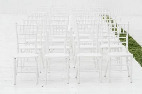 Rows of empty white chairs sitting on a wooden floor. Wedding chairs with Stock Photos