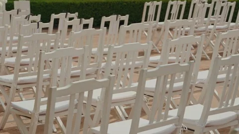 Rows of empty white folding chairs set up for outdoor ceremony Stock Footage 346153650