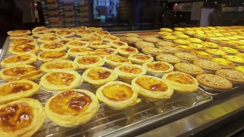 Rows of freshly baked Portuguese egg tarts are displayed on cooling racks Stock Footage 340864868