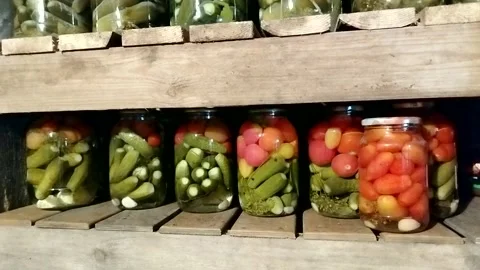 Rows of glass jars with pickled cucumbers and tomatoes on a wooden cellar shelf  Stock Footage 326134937