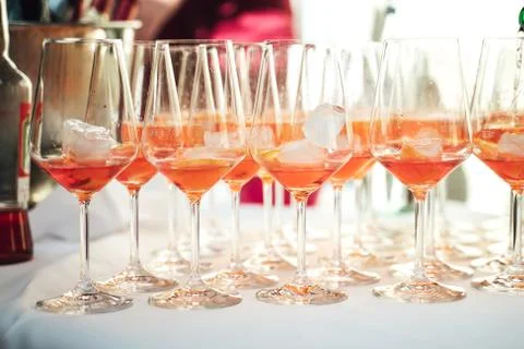 Rows of glasses with orange drink and ice cubes standing on buffet table Stock Photos