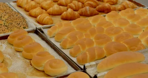 Rows of golden bakery rolls on metal trays in commercial kitchen baking area Видео 345666342