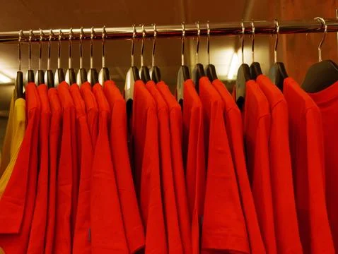 Rows of identical red shirts hanging on hangers in apparel store Stock Photos