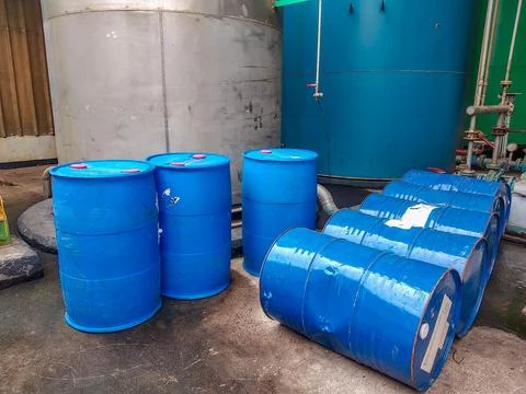Rows of large blue plastic barrels are arranged near industrial equipment Stock Photos