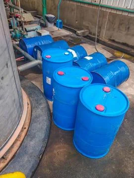 Rows of large blue plastic barrels are arranged near industrial equipment Stock Photos