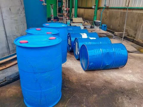 Rows of large blue plastic barrels are arranged near industrial equipment Stock Photos