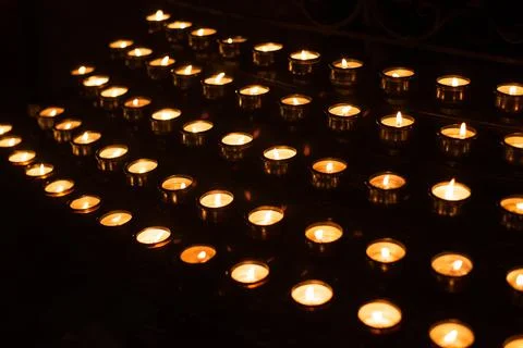 Rows of lighted prayer candles in the darkness in a church Stock Photos