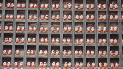 Rows of numerous traditional Daruma dolls are arranged on rustic wooden shelves Stock Footage 344281894