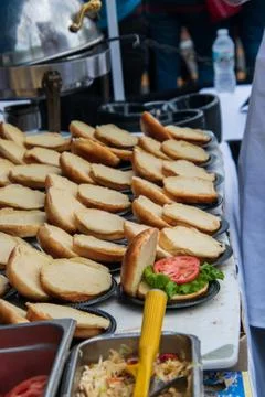 Rows of opened hamburger buns on a table. Only one had lettuce and a slice of Stock Photos