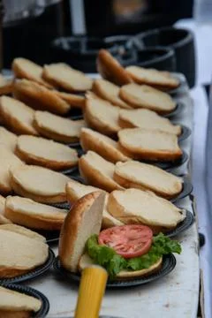Rows of opened hamburger buns on a table. Only one had lettuce and a slice of Stock Photos