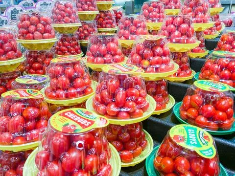 Rows of packaged red cherry tomatoes in plastic containers on display at a .. Foto stock